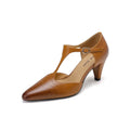 Brown retro women's T-strap sandals with a closed toe, low upper, and a stout high heel on a wooden floor.