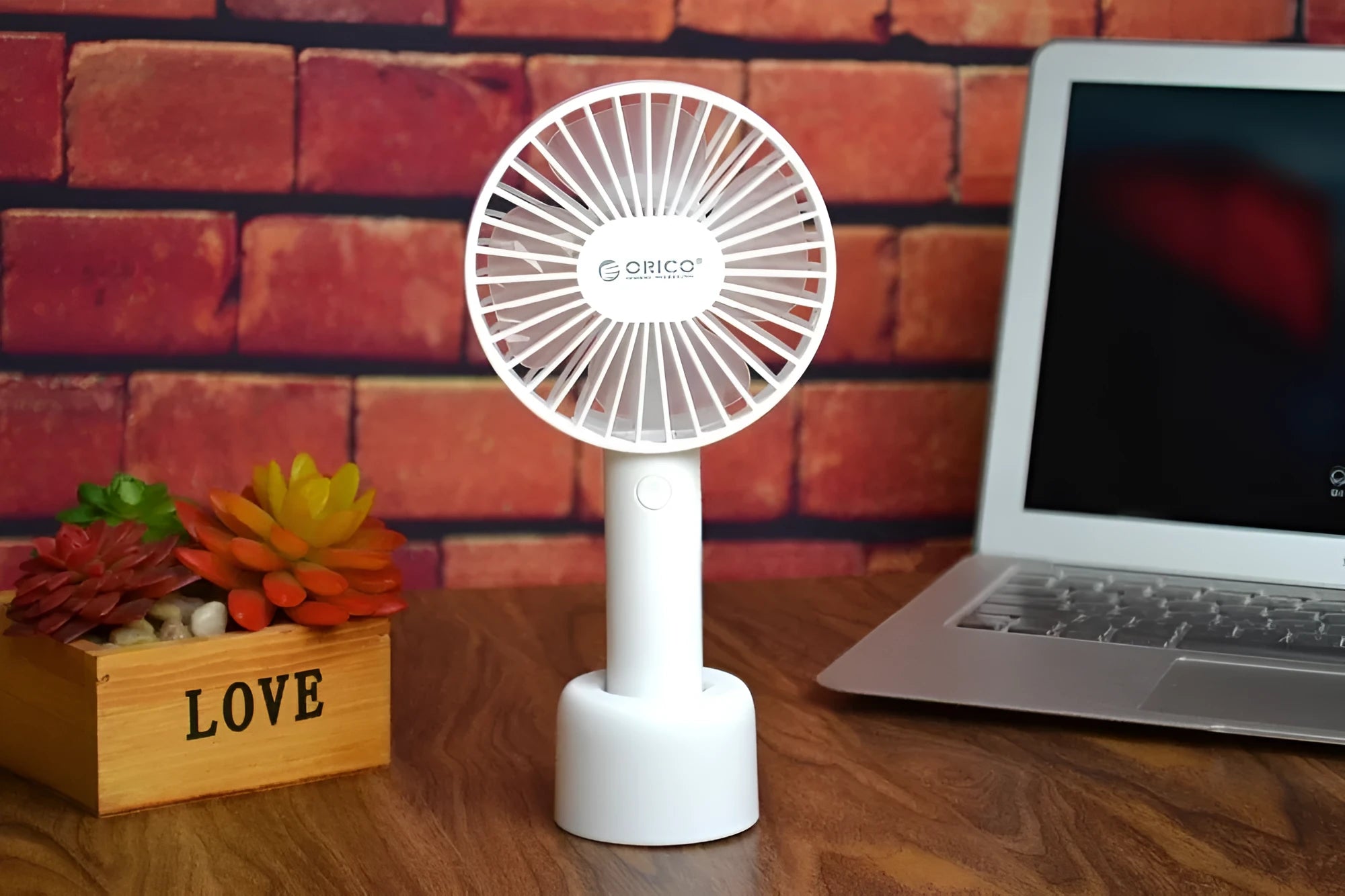 White ORICO FH1 portable USB desk and handheld fan with rechargeable battery on a wooden table.