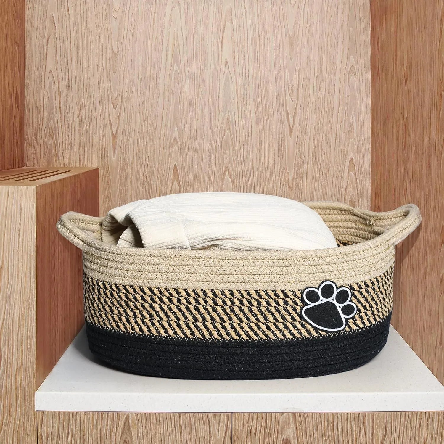 Light beige handmade woven cotton rope storage basket with wooden handle on a table.