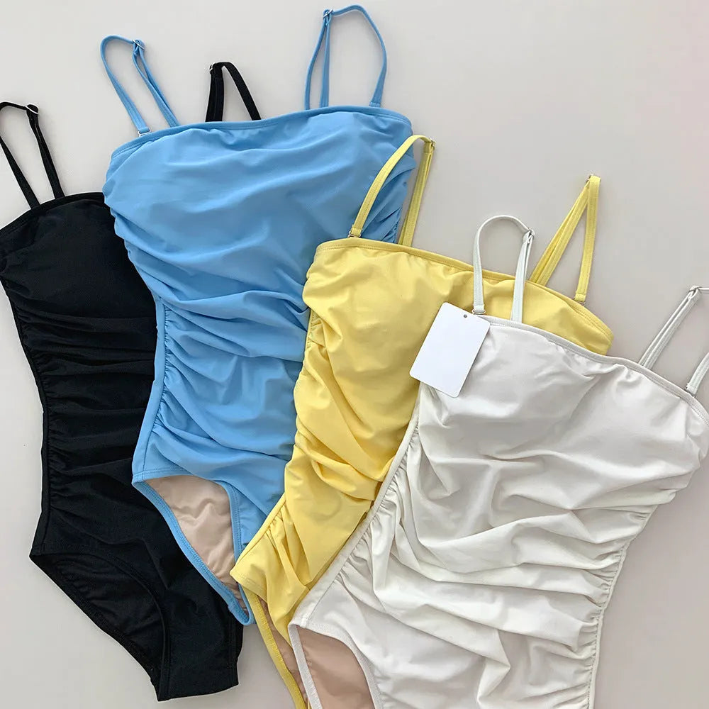Blue one-piece swimsuit with sling neckline and pleating detail across the belly.