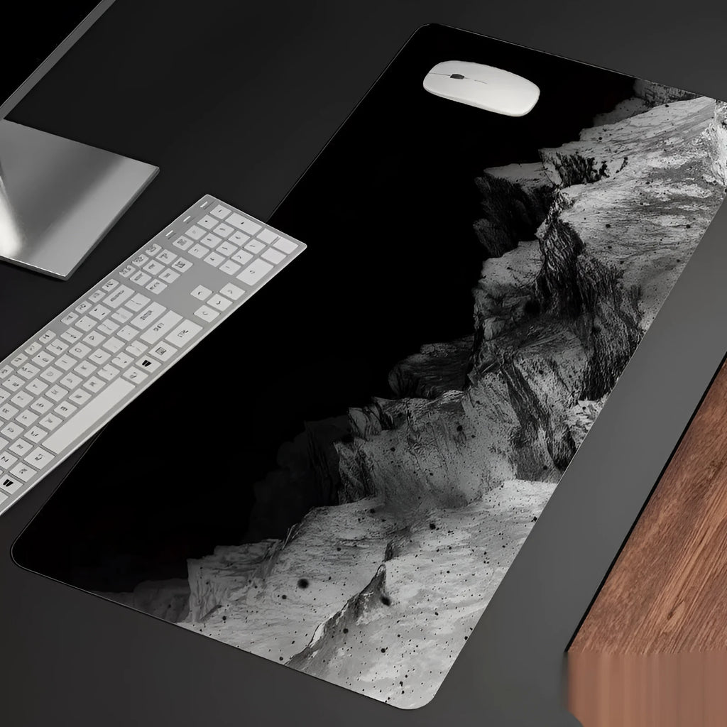 Oversized black gaming mouse pad with printed design and integrated raised wrist rest on a desk.