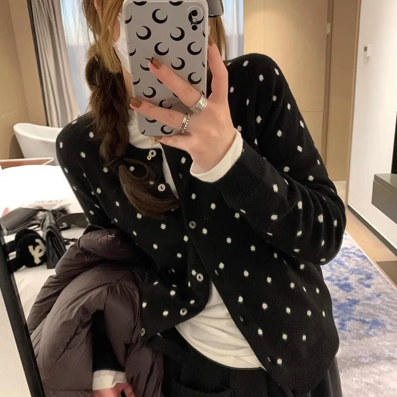 Grey dot patterned women's knitted cardigan with crochet flower detail on a hanger.