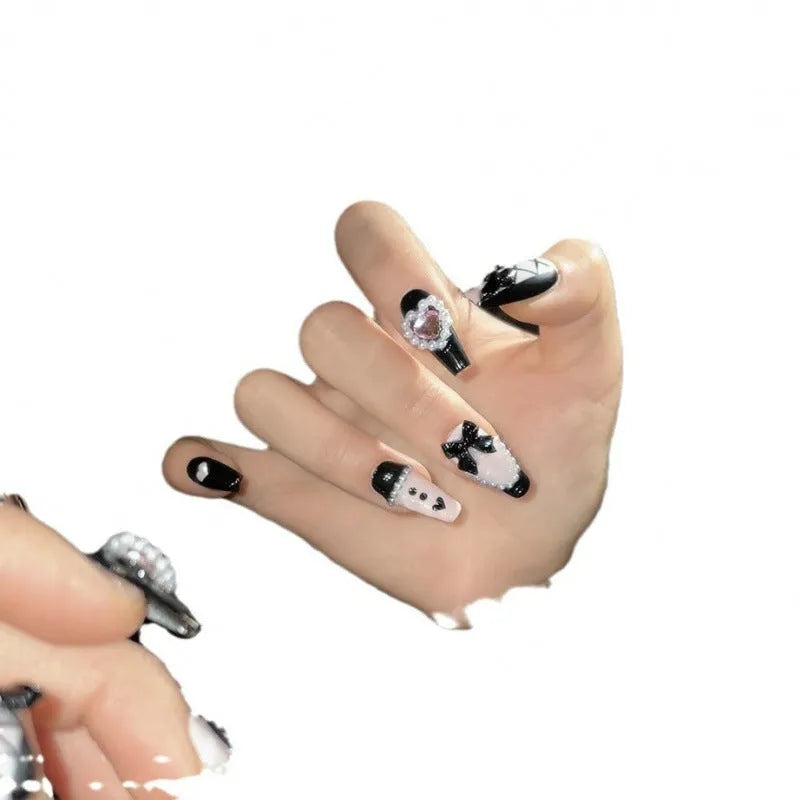 Hand-painted black false nails with pink peach hearts, XINGX text, bows, and a cat's eye shimmer effect.