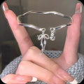 Silver bow bracelet with adjustable bell clasp on wrist, showing M1534 electroplated finish
