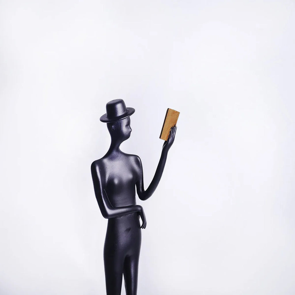 Black aluminium desktop sculpture of reading woman figure measuring 12x12x51cm