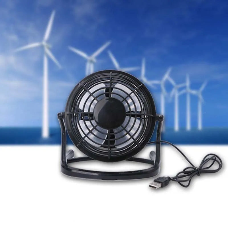 Compact black USB desk fan with adjustable tilt angle on a wooden desk next to a laptop