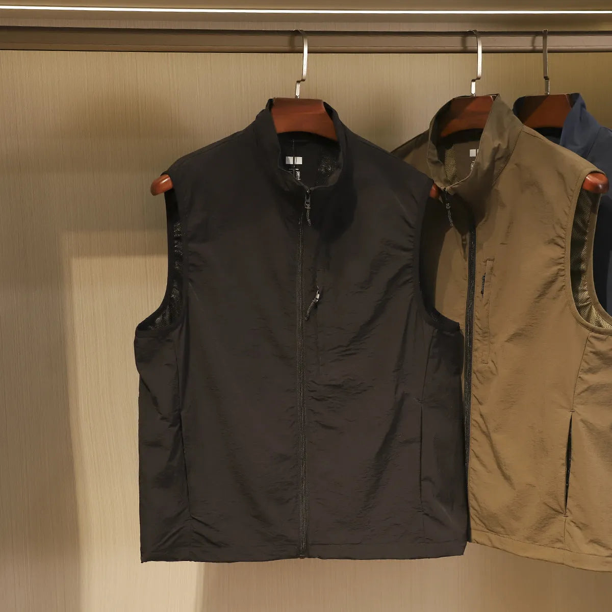 Men's straight cut nylon vest in army green with side seam pockets on a hanger.