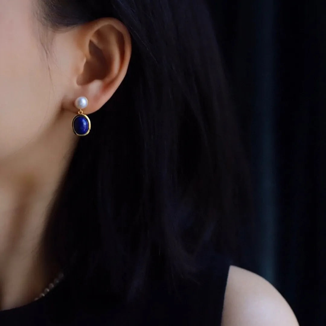 A pair of simple stud earrings with blue lapis lazuli pearls set in silver backings featuring auspicious patterns.