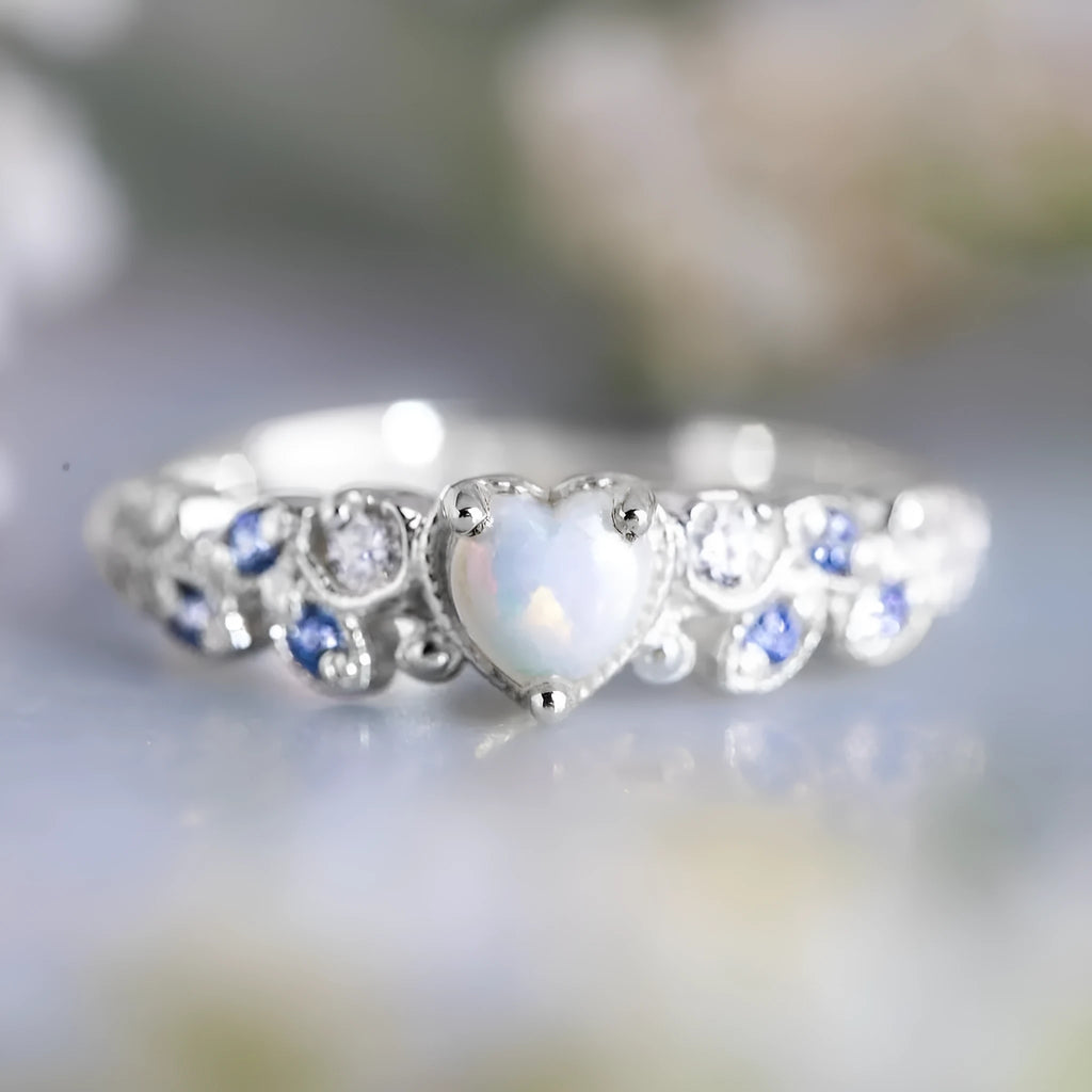 White electroplated women's ring with a peach-coloured heart shape, shown on a finger.