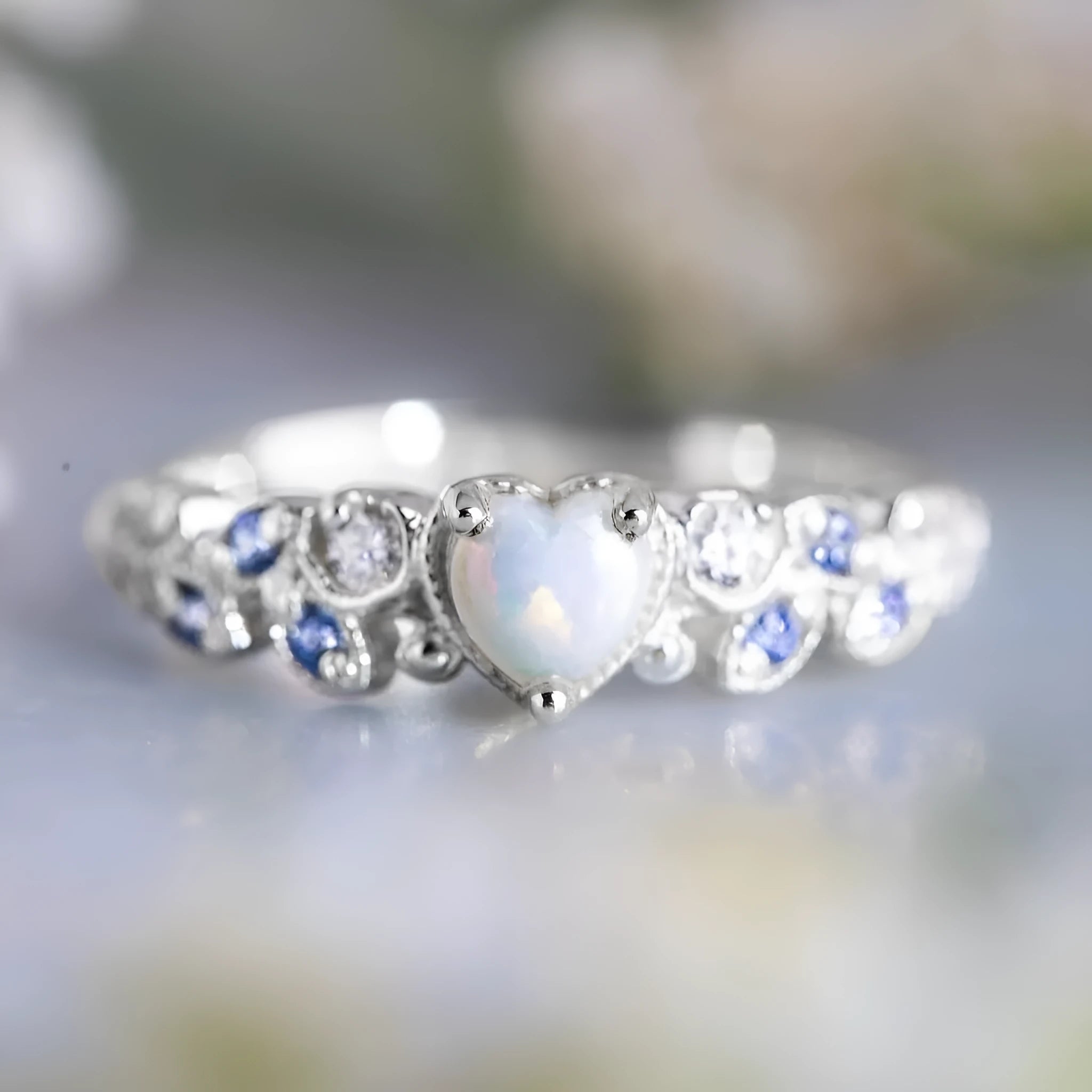 White electroplated women's ring with a peach-coloured heart shape, shown on a finger.