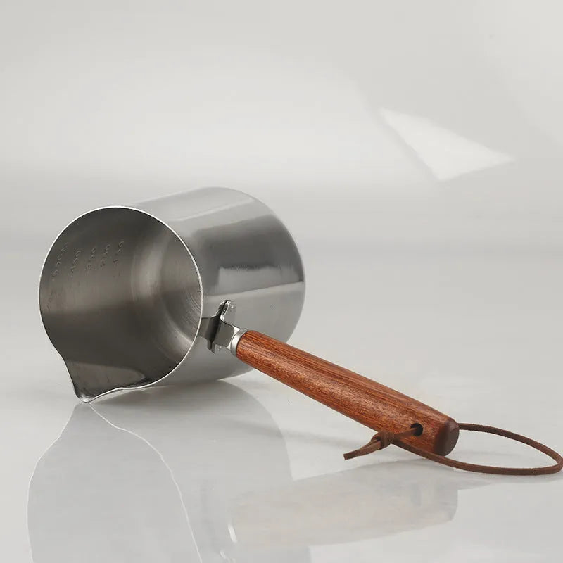Stainless steel coffee cup with wooden handle showing interior measurement scale for latte art