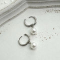 A pair of geometric pearl-coloured alloy earrings with titanium steel posts on a white background.