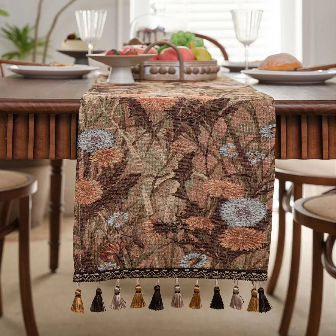 Long beige jacquard table runner with floral pattern and tassels on a wooden dining table.