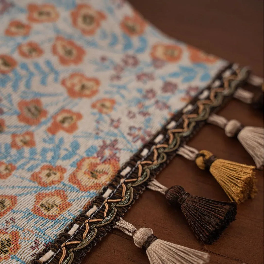 Long beige jacquard table runner with floral pattern and tassels on a wooden dining table.
