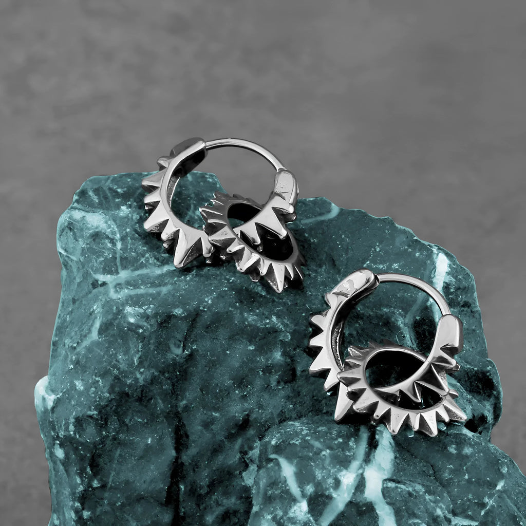 A pair of polished steel-coloured stainless steel round ring earrings on a simple background.