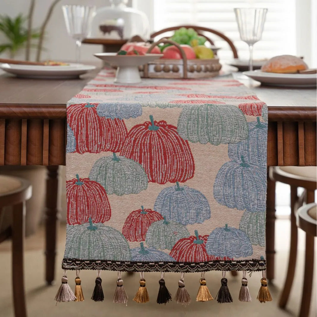 Long beige jacquard table runner with floral pattern and tassels on a wooden dining table.