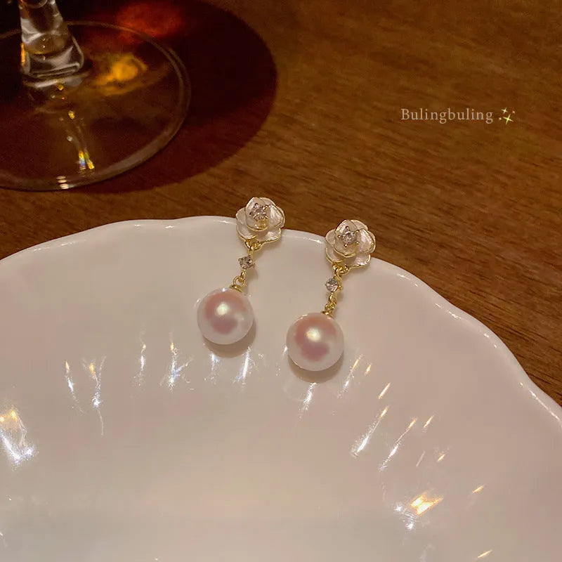 A pair of camellia flower stud earrings for women with a pearl centre, made from alloy.