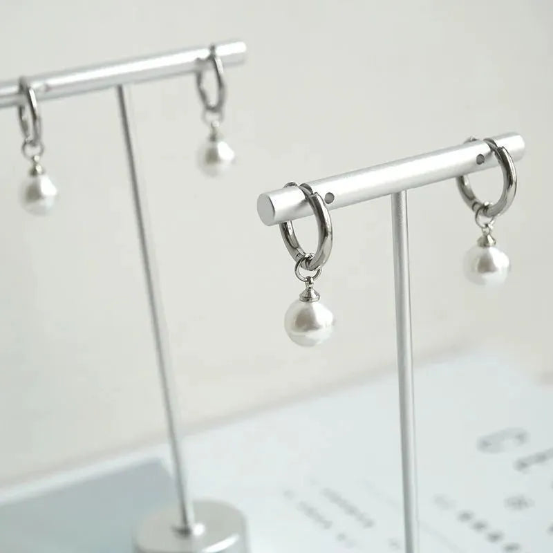 A pair of geometric pearl-coloured alloy earrings with titanium steel posts on a white background.