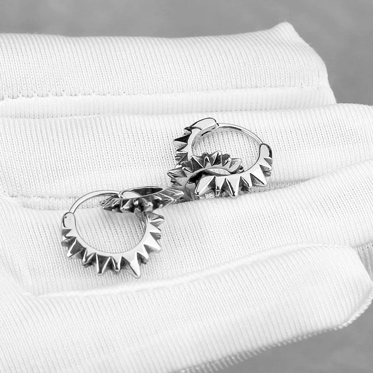 A pair of polished steel-coloured stainless steel round ring earrings on a simple background.