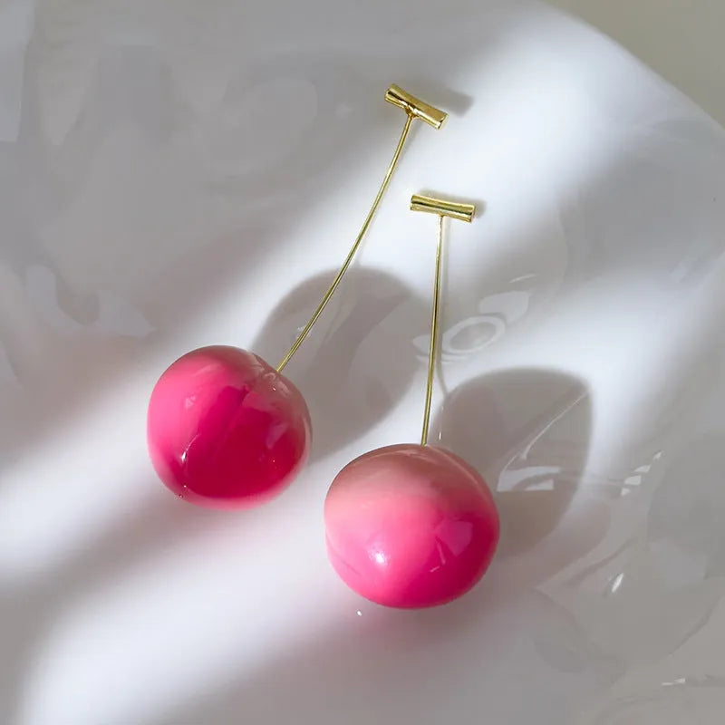 A pair of acrylic peach-shaped dangle earrings with copper hooks, shown in two size variants.