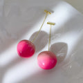 A pair of acrylic peach-shaped dangle earrings with copper hooks, shown in two size variants.