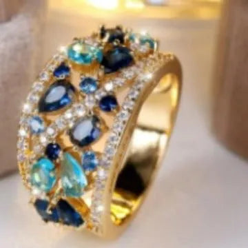 Women's hollow round fashion ring in gold tone with blue stones, showing openwork design.