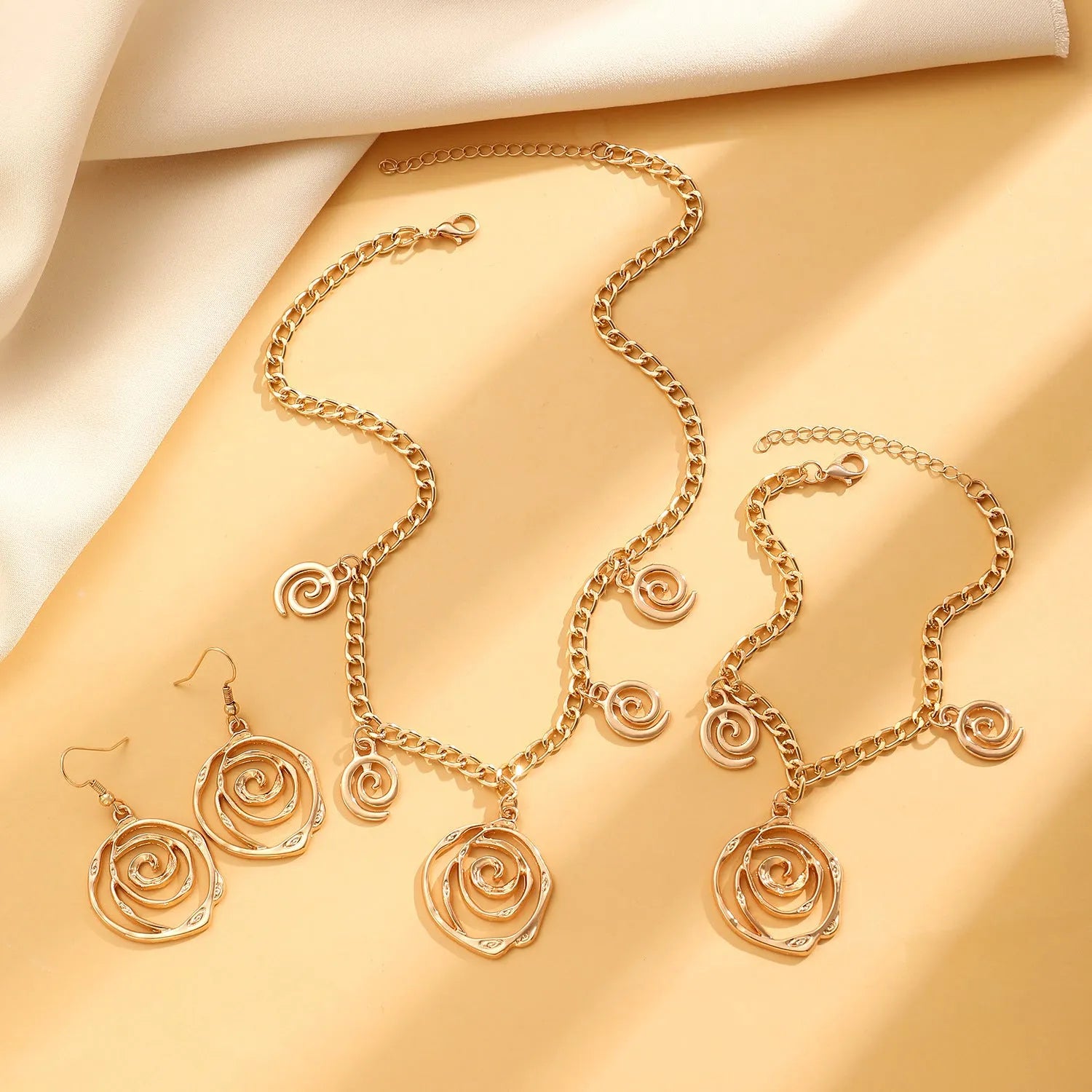 Gold tone spiral donut design necklace, bracelet, and earrings set on a white background.