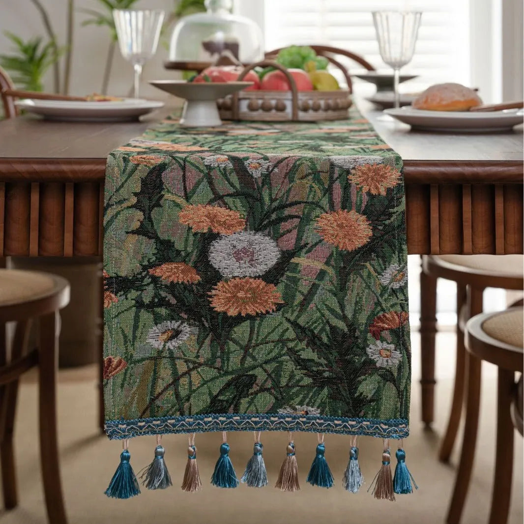 Long beige jacquard table runner with floral pattern and tassels on a wooden dining table.