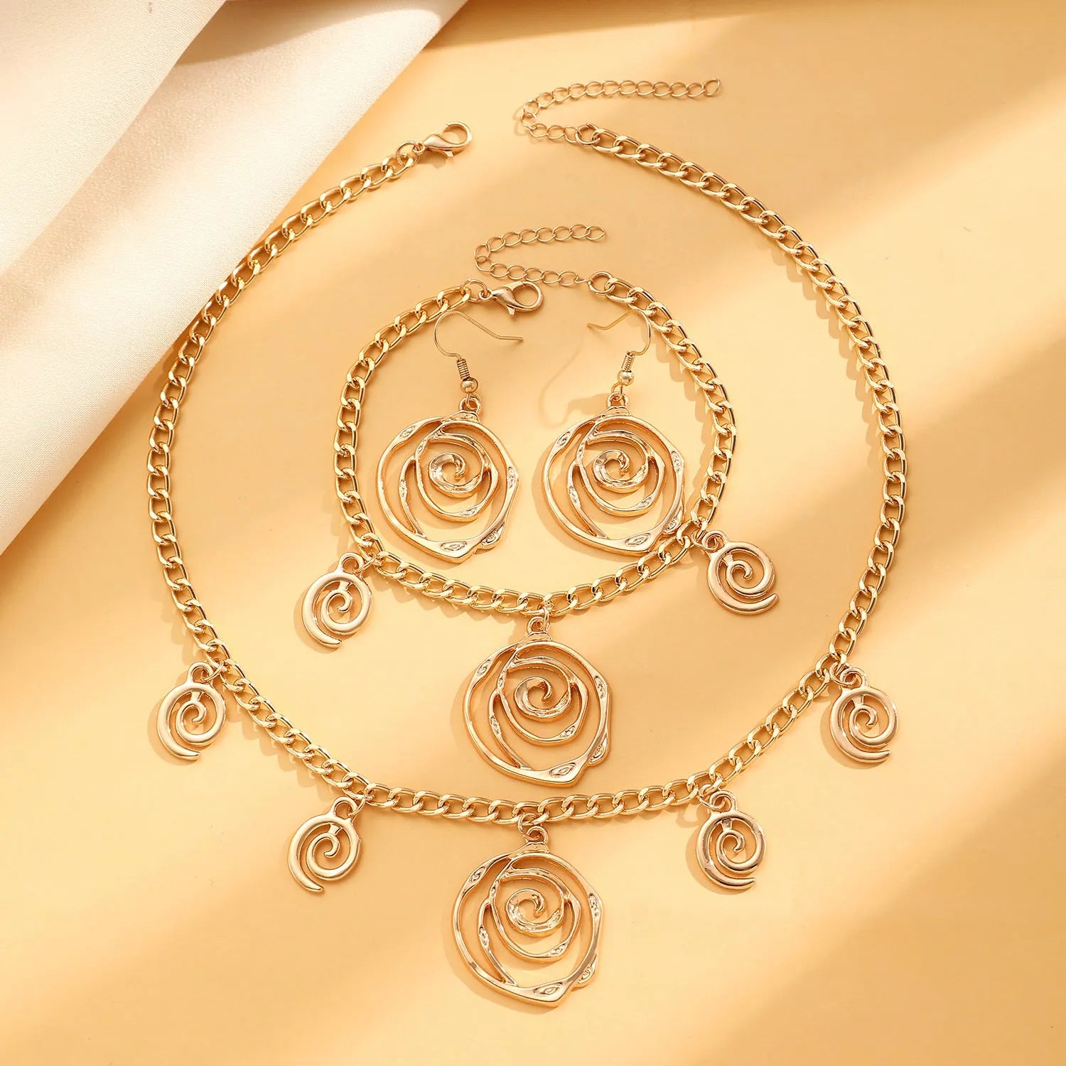 Gold tone spiral donut design necklace, bracelet, and earrings set on a white background.