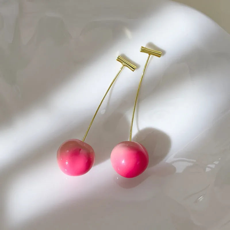 A pair of acrylic peach-shaped dangle earrings with copper hooks, shown in two size variants.