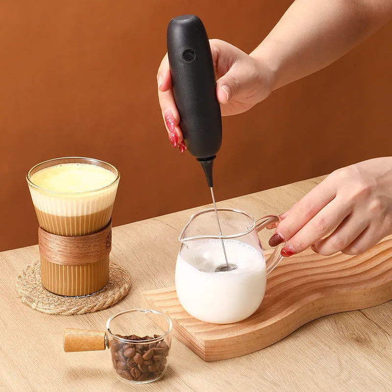 A black and a white hand-held electric milk frother for coffee, displayed on a kitchen counter.