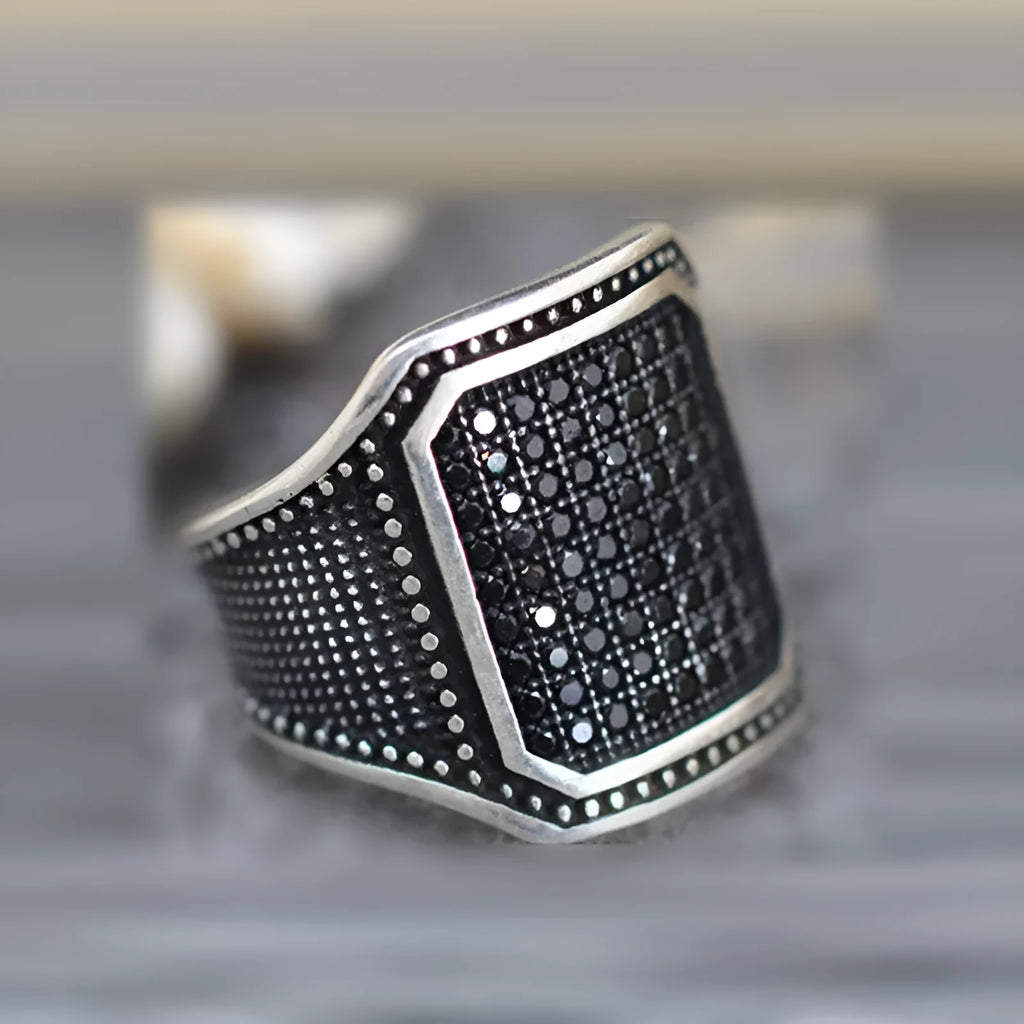 Black alloy ring with copper inlays holding zircon stones, shown on a finger.