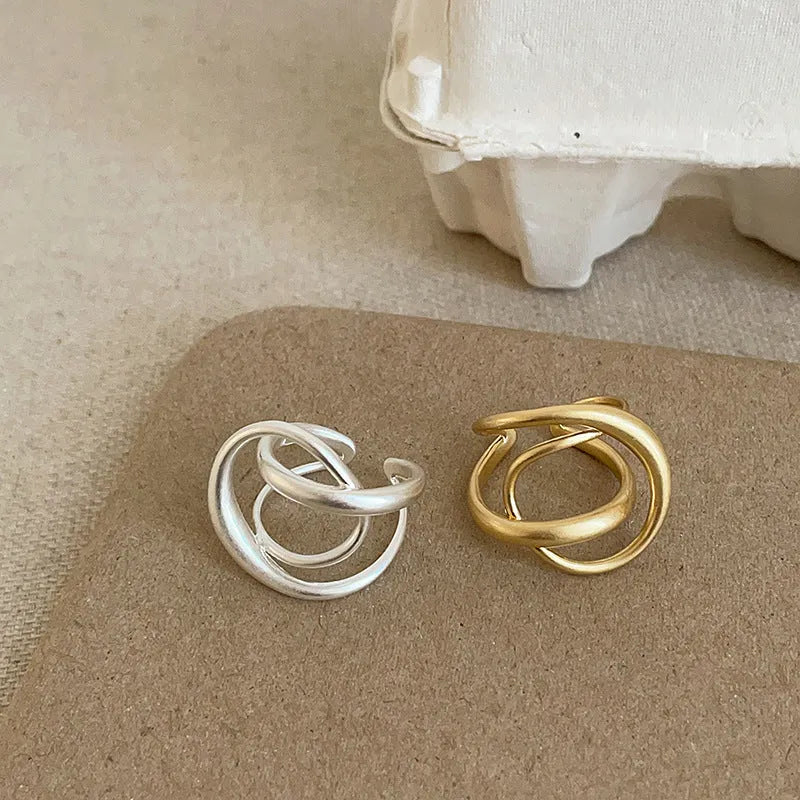 Geometric open ring for women with three-dimensional interlaced design in matte gold or silver metal.