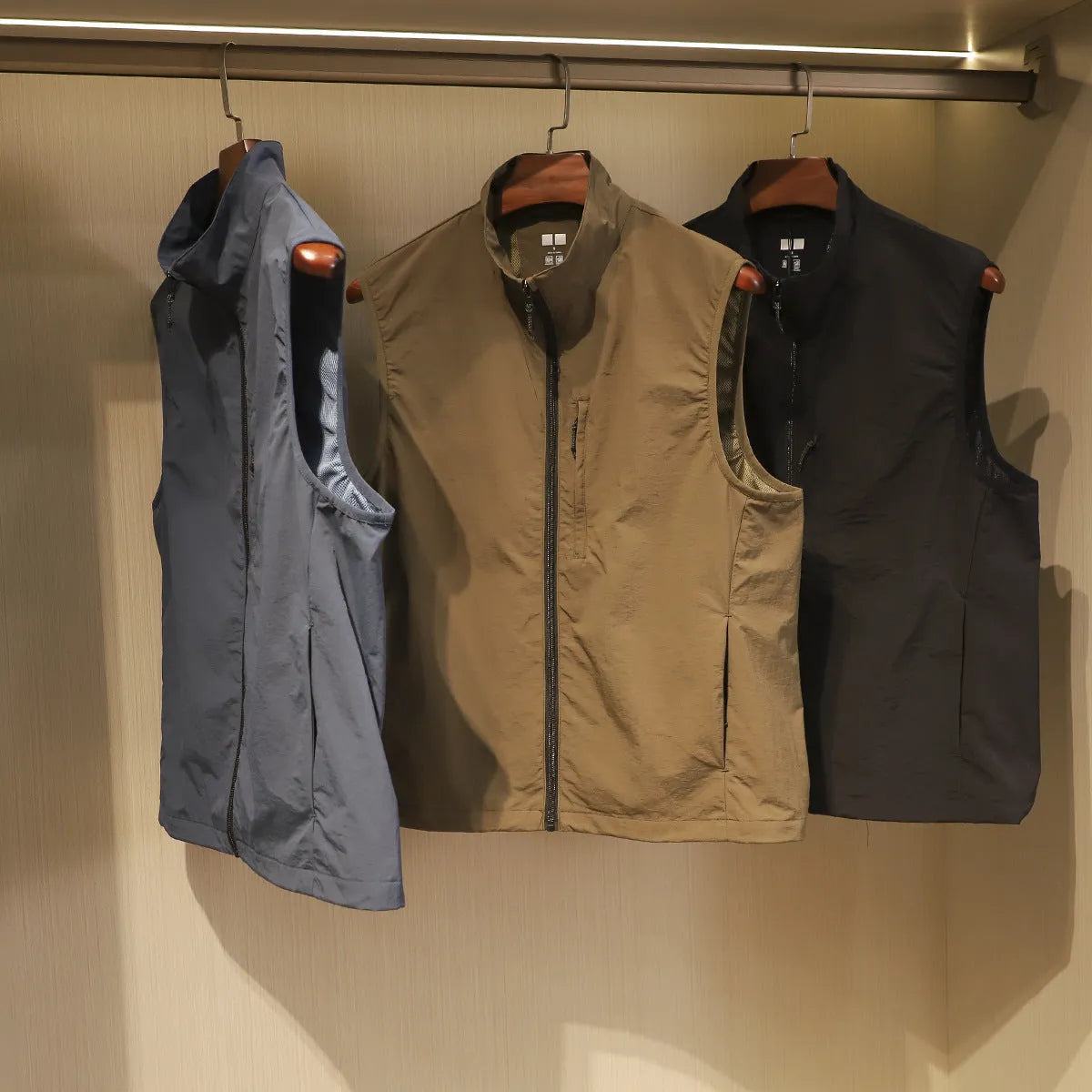 Men's straight cut nylon vest in army green with side seam pockets on a hanger.
