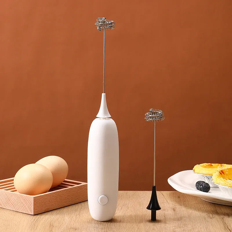 A black and a white hand-held electric milk frother for coffee, displayed on a kitchen counter.