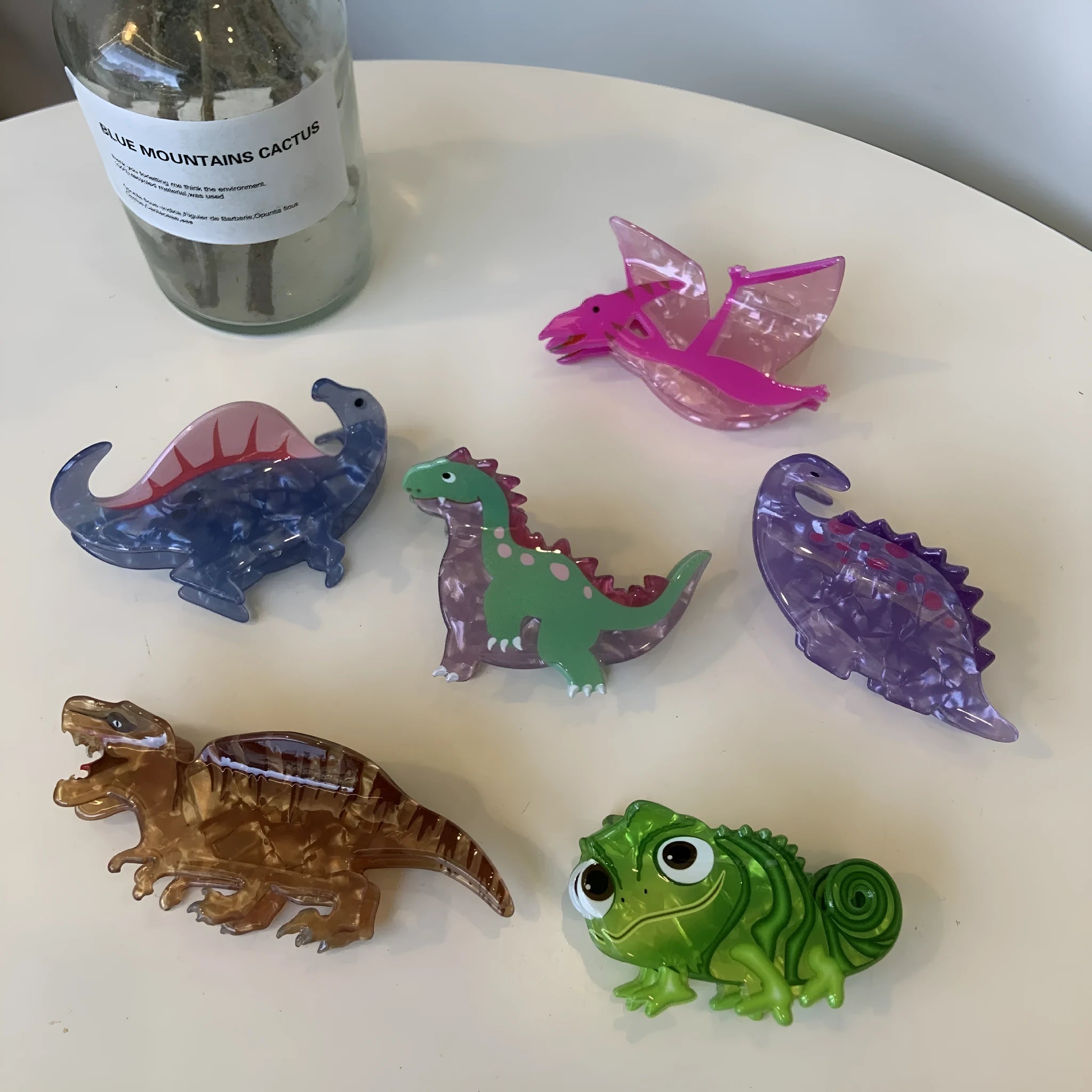 Dinosaur acrylic jaw clip hairpin showing colourful dinosaur designs including pink pterosaur and green stegosaurus