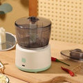 White mini electric meat grinder with transparent cup and stainless steel blades on a kitchen worktop