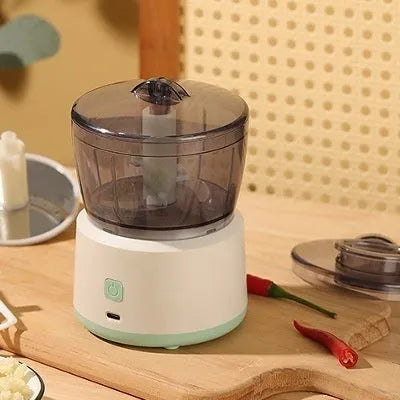 White mini electric meat grinder with transparent cup and stainless steel blades on a kitchen worktop