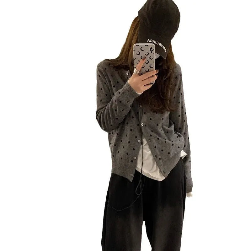 Grey dot patterned women's knitted cardigan with crochet flower detail on a hanger.