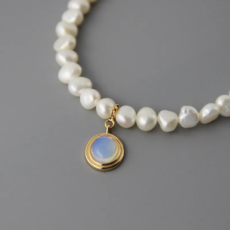 Round medal pearl necklace with geometric silver pendant and irregular pearls on a silver chain.