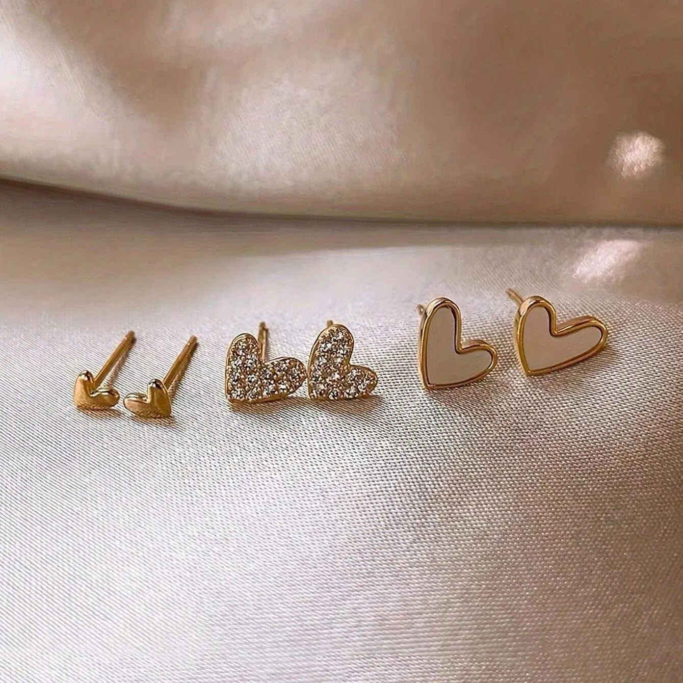 Three pairs of heart-shaped girly earrings in gold, black, black and white, and pink colours