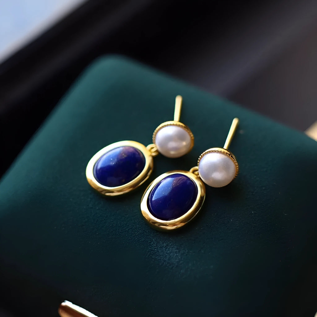 A pair of simple stud earrings with blue lapis lazuli pearls set in silver backings featuring auspicious patterns.