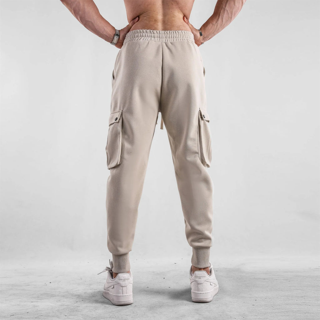 Men's loose light grey cotton sports trousers with ankle ties and multiple pockets laid flat.