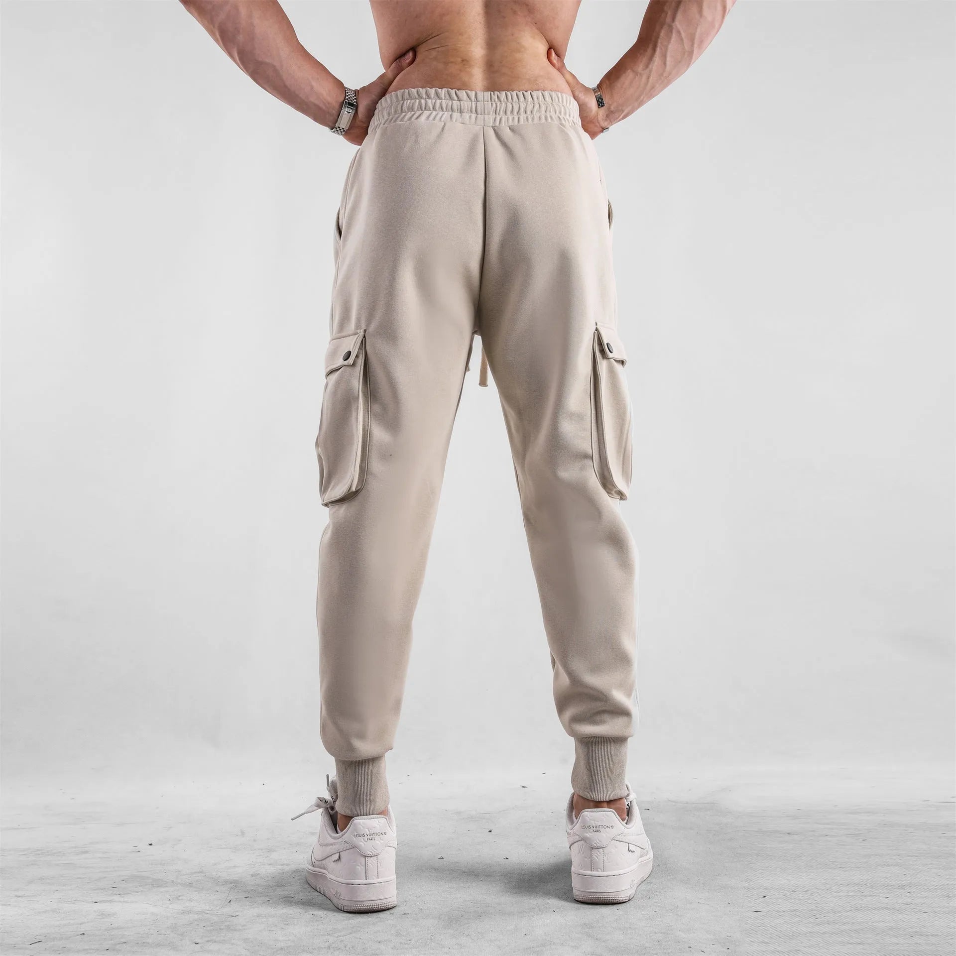 Men's loose light grey cotton sports trousers with ankle ties and multiple pockets laid flat.