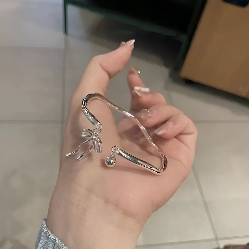 Silver bow bracelet with adjustable bell clasp on wrist, showing M1534 electroplated finish