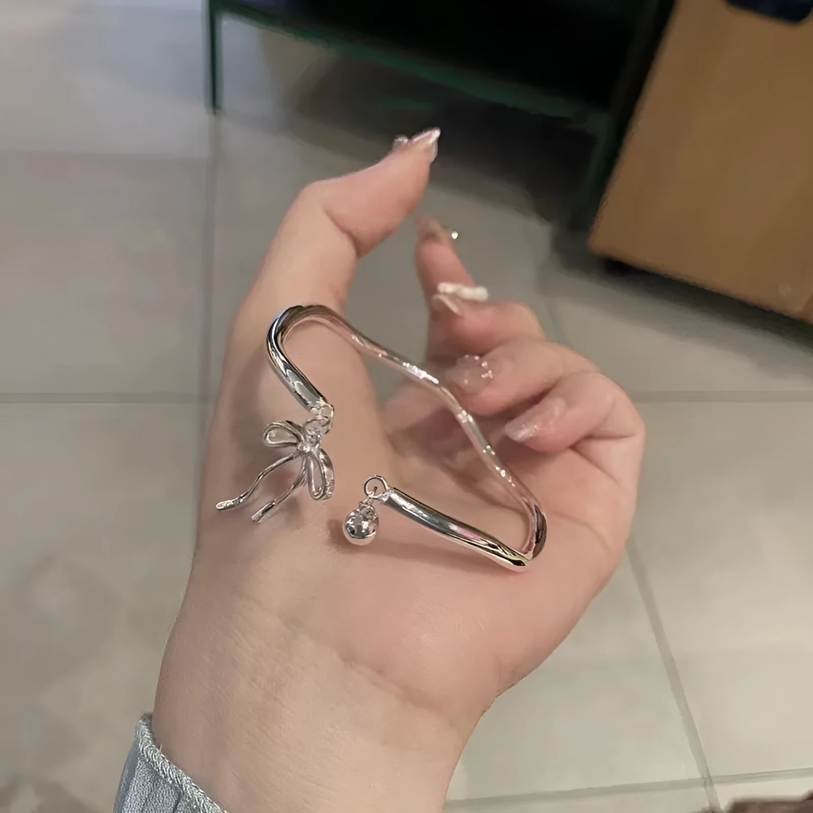 Silver bow bracelet with adjustable bell clasp on wrist, showing M1534 electroplated finish