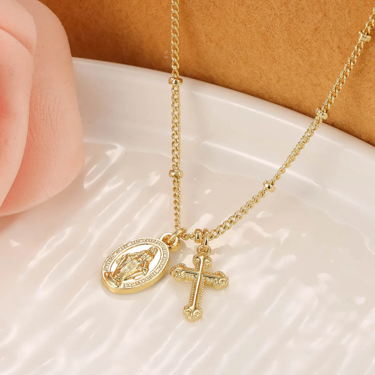 Gold geometric cross pendant necklace with Virgin Mary design on a chain.