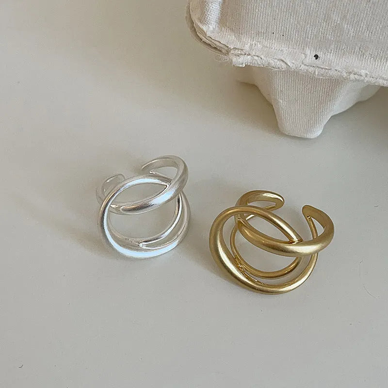 Geometric open ring for women with three-dimensional interlaced design in matte gold or silver metal.