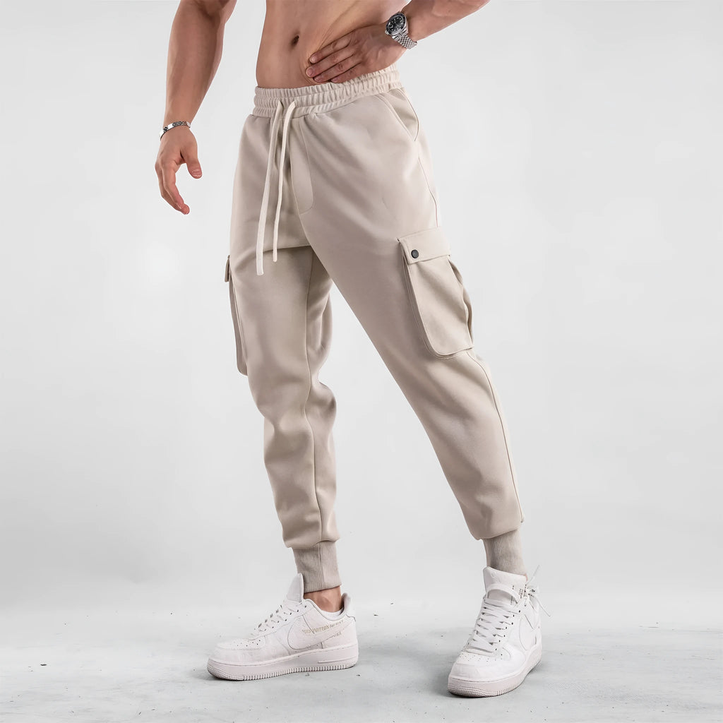 Men's loose light grey cotton sports trousers with ankle ties and multiple pockets laid flat.