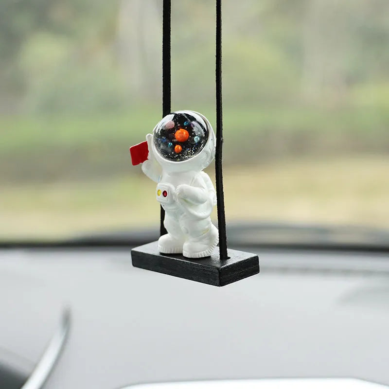 Resin cartoon astronaut car pendant charm in red flag design hanging from a rearview mirror.